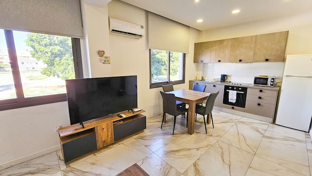 Eine moderne Küche mit Einbauofen, Mikrowelle und Kühlschrank. Ein Essbereich mit Tisch und Stühlen, sowie ein Flachbildfernseher an einem Holzkabinett.