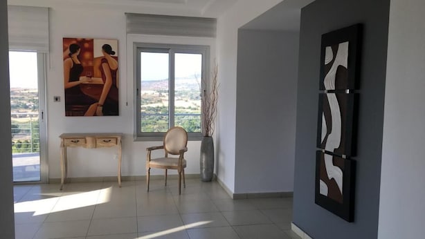 Una habitación con un ventanal grande, un escritorio de madera, una silla y dos cuadros abstractos en la pared.