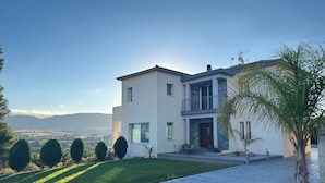 Una casa moderna de dos pisos con entrada pavimentada, un pequeño patio y vistas del paisaje circundante.