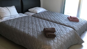 Una cama doble con edredón gris acolchado, dos almohadas y toallas dobladas en la cabecera.