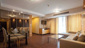 A modern hotel room with a glass dining table, a sofa, a kitchen area, and a large window with curtains. - 5A - 2 Bedroom Downtown Apartment With Shared Pool (Bangkok)