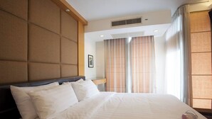 A hotel room with a large bed, a headboard, a bedside table, and a window with curtains. - 5A - 2 Bedroom Downtown Apartment With Shared Pool (Bangkok)