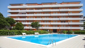 Un hotel de varios pisos con piscina, balcones blancos y un paseo con baldosas.