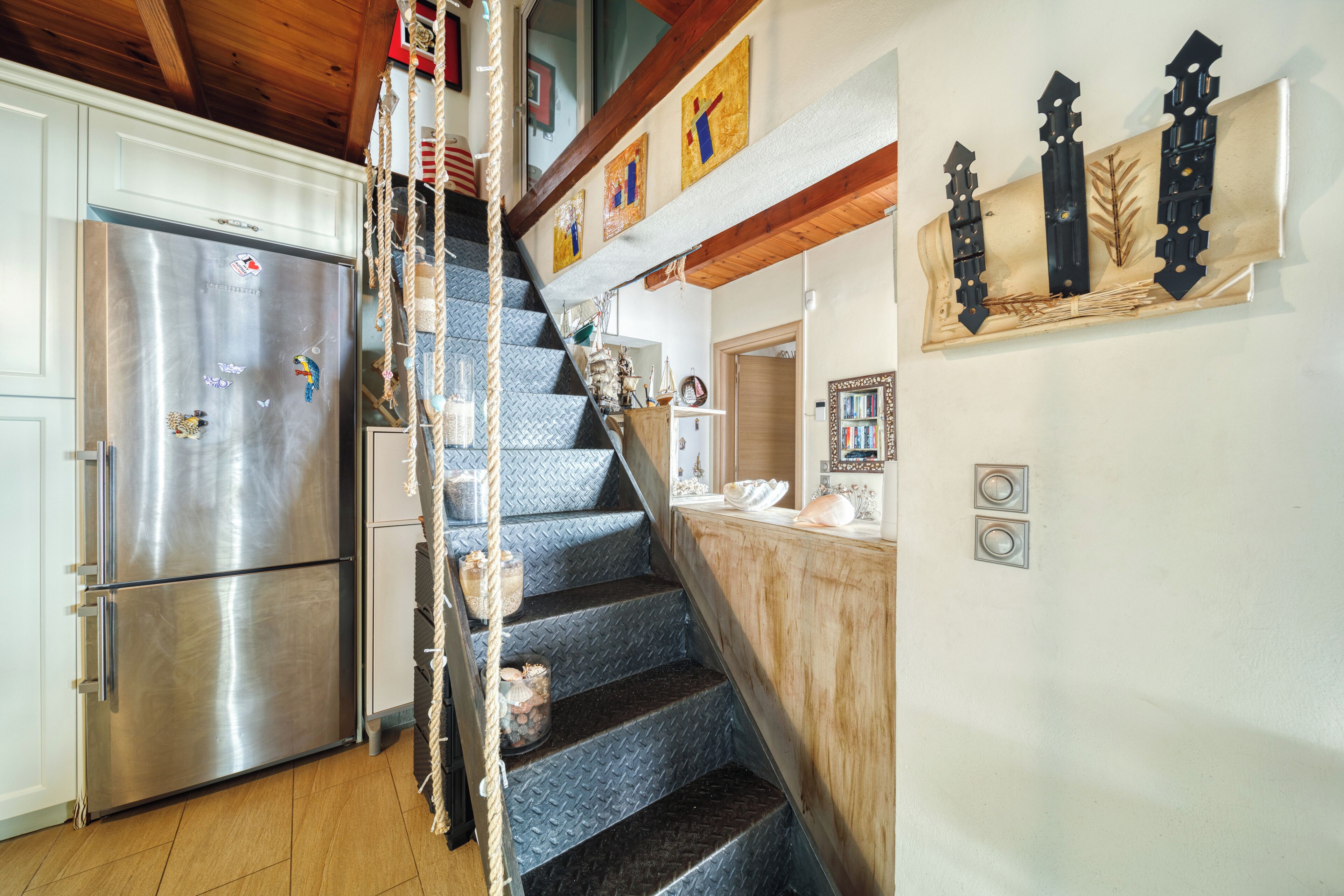 A kitchen with a stainless steel refrigerator, a wooden staircase, and a decorative wall piece.