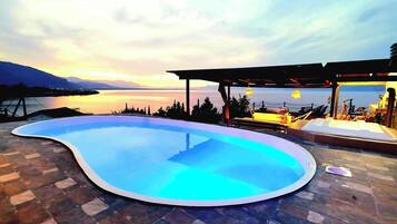 A swimming pool with a curved edge, surrounded by a stone patio.