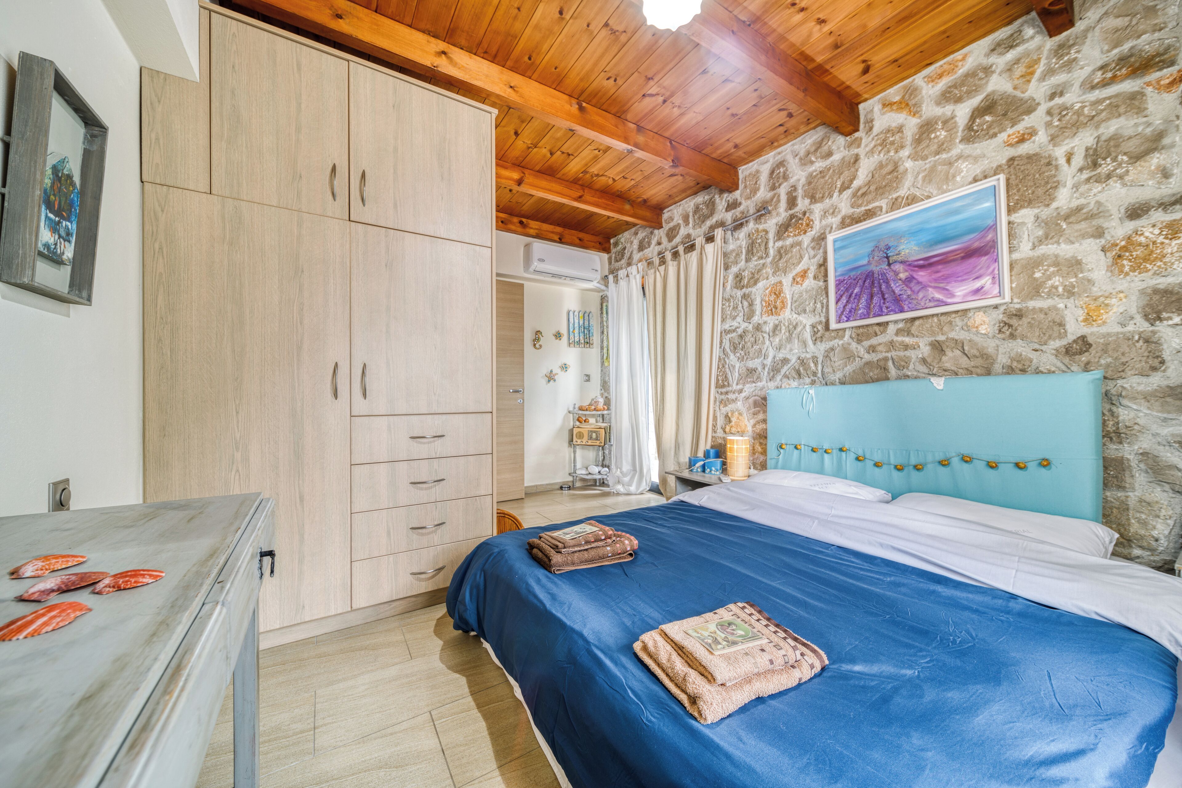 A bedroom with a stone wall, wooden ceiling, and a bed with a blue bedspread.