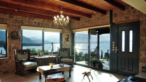 Ein Zimmer mit einer Steinwand, Holzbalkendecke, einem Chandelier, Meerblick, einem Esstisch und einer Couch.