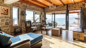 Ein geräumiges Zimmer mit Steinwand, Holzboden und großen Fenstern mit Blick aufs Meer.