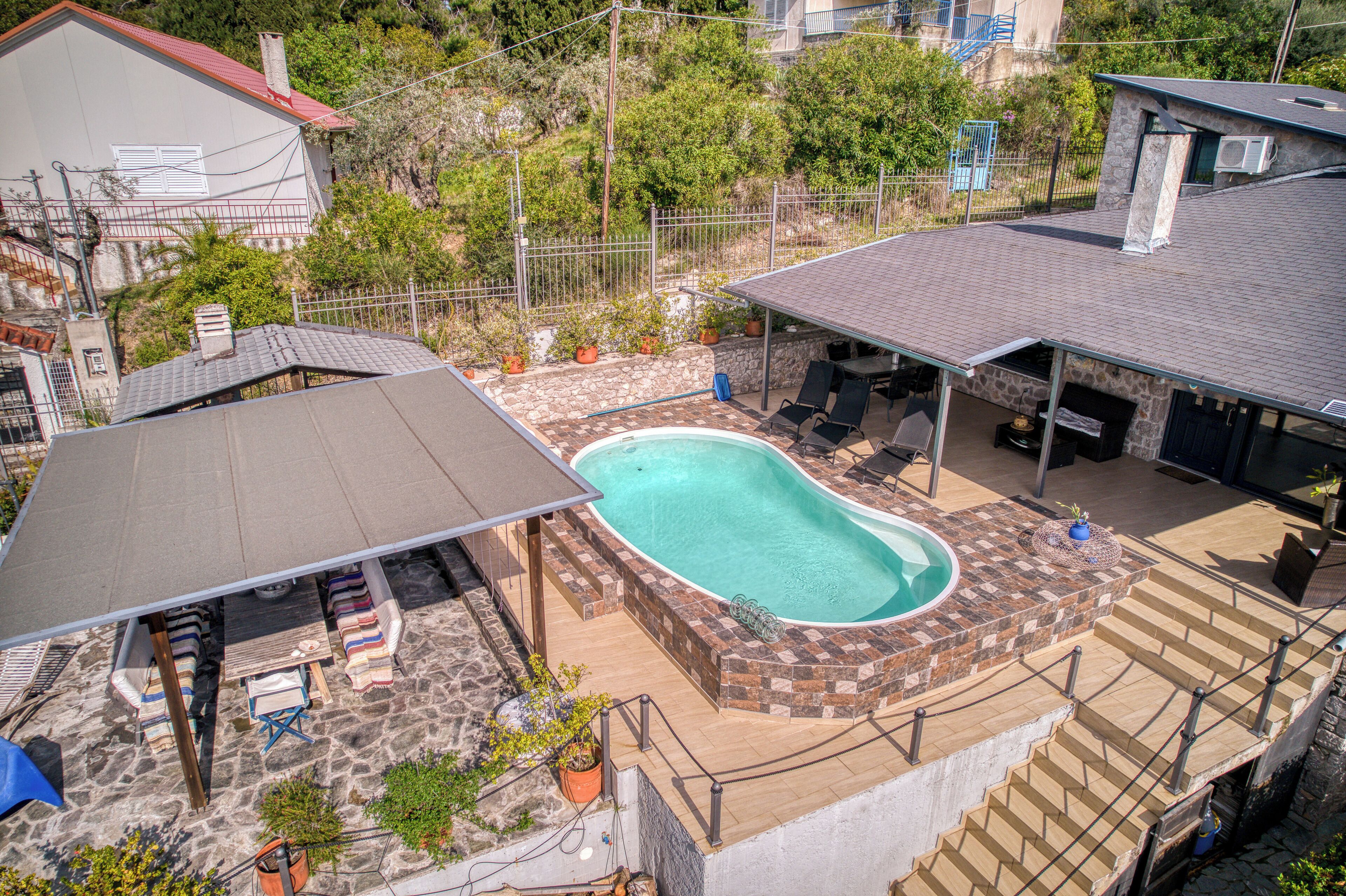 Una propiedad residencial con piscina, mobiliario exterior y un patio de piedra.