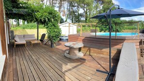 Eine Holzterrasse mit Pool, Sitzgelegenheiten im Freien und einer Pergola.