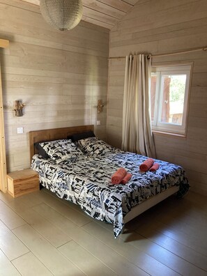 Een kamer met een bed, houten wanden, een raam met gordijnen en een hanglamp.