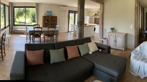 Ein geräumiges Wohnzimmer mit einem dunkelgrauen Sofa, einem Fernseher und einem Essbereich mit Tisch und Stühlen.