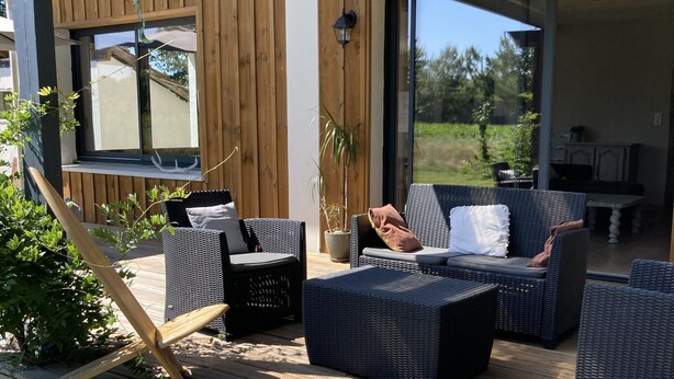 Eine Terrasse im Freien mit Korbmöbeln, ein Holzdeck und Blick auf die Umgebung.
