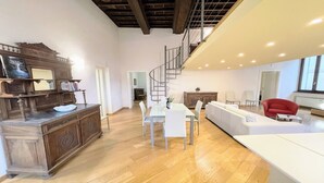 A spacious living area with a wooden dining table, white chairs, a white sofa, and a red armchair. A spiral staircase leads to an upper level. - Central Spoleto 6 Guests apt With Terrace (Spoleto)