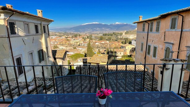 A balcony with a table and chairs, overlooking a town with buildings and a mountain in the distance. - Central Spoleto 6 Guests apt With Terrace (Spoleto)