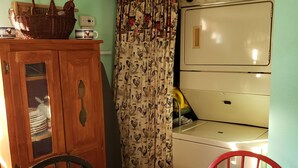 A dining area with a table covered in a rooster-patterned tablecloth, a red chair, a wooden cabinet, and a vintage stove.
