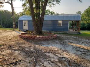 A single-story house with a metal roof, a brick planter around a tree, and a porch with outdoor seating.