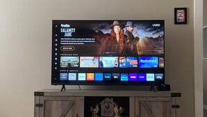 A flat-screen TV mounted on a wooden cabinet with a 'Welcome to our FARMHOUSE' sign below it.