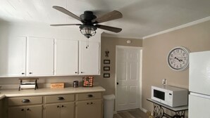 A kitchen with white cabinets, a ceiling fan, a microwave, and a clock on the wall.