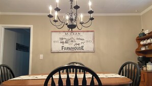 A dining room with a chandelier, a farmhouse sign, and wooden furniture.