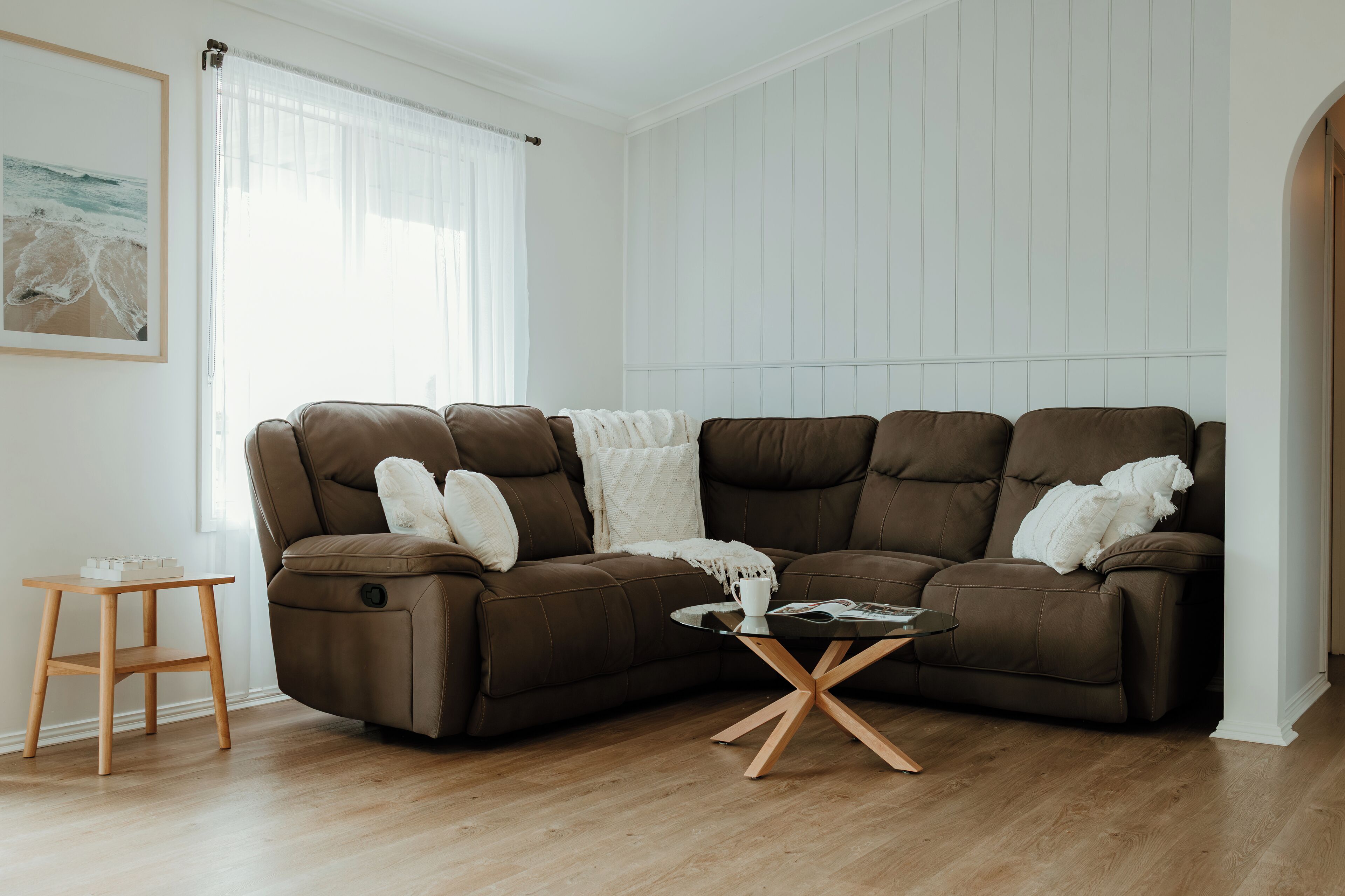 Ein modernes Wohnzimmer mit einem braunen Ecksofa, einem kleinen Holznachttisch und einem Glastisch.