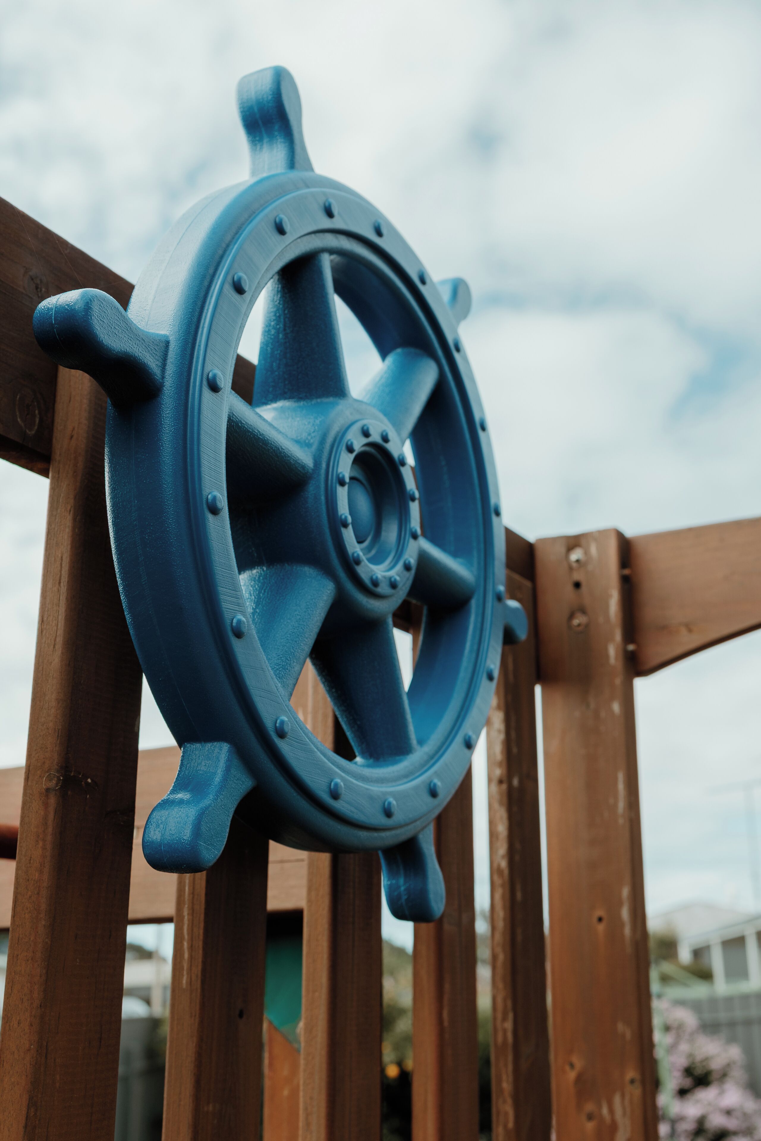 A close-up of a blue ship's wheel mounted on a wooden structure.