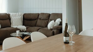 Ein modernes Wohnzimmer mit einem braunen Ledersofa, einem Holzesstisch mit einer Weinflasche und einem Glas sowie einer geometrischen Pendelleuchte.