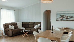 Ein modernes Wohnzimmer mit einem braunen Sofa, weißen Stühlen, einem Holzesstisch und einem Bild von Booten an der Wand.