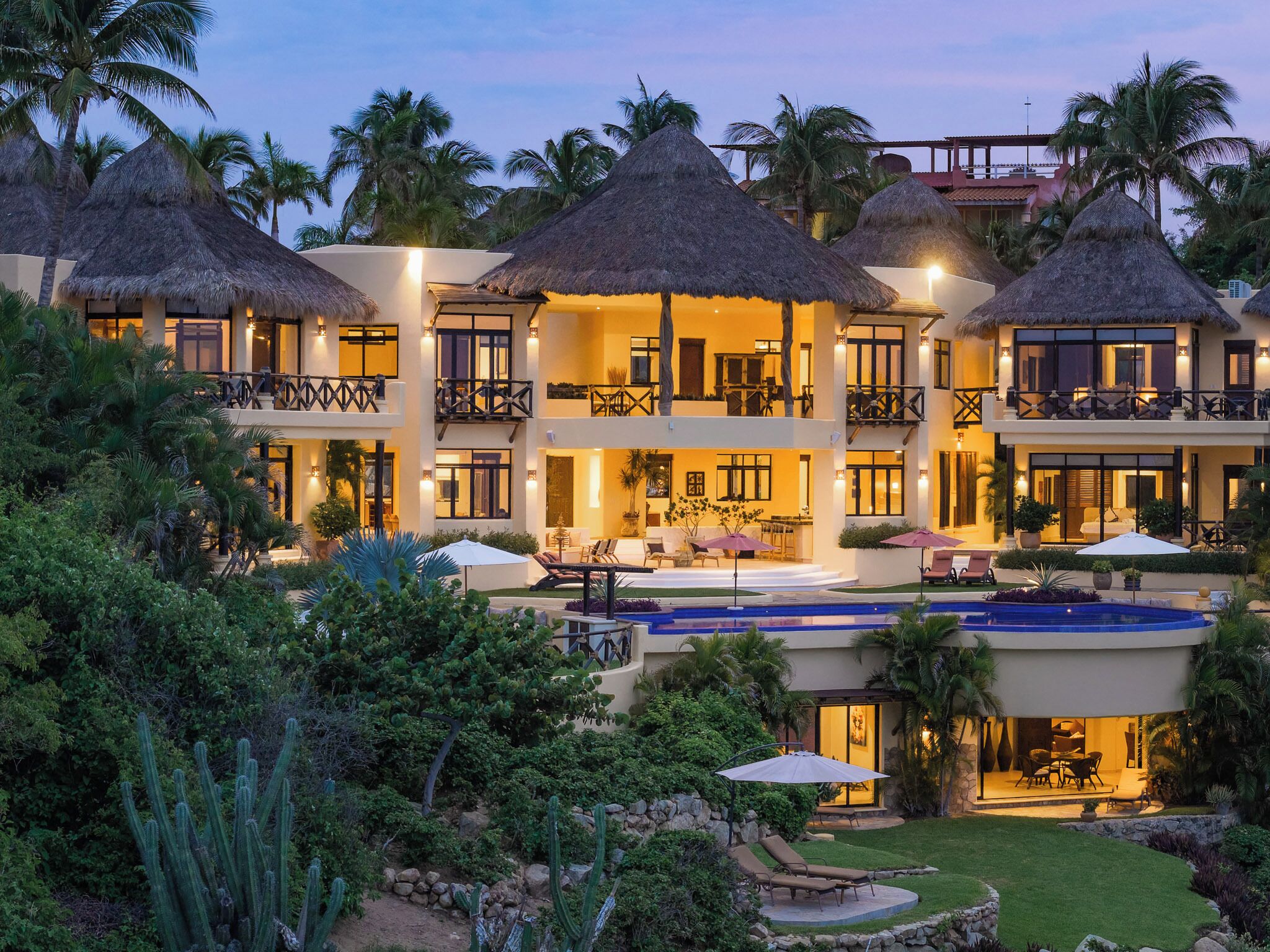 A resort with multiple thatched-roof structures, a swimming pool, and lush landscaping.