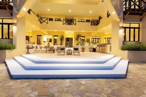 A hotel lobby with a central seating area, a staircase leading to the upper floor, and a bar area.