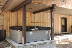 A wooden cabin with a hot tub under a covered porch.
