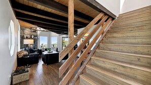 Eine Holztreppe führt zu einer oberen Ebene mit einem Steinkamin und einer gemütlichen Sitzecke darunter.