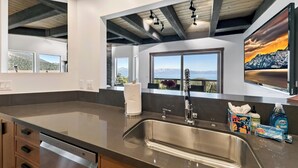 Eine moderne Küche mit Spüle aus Edelstahl, Holzschränken und einem großen Fenster mit Blick auf die Berge.