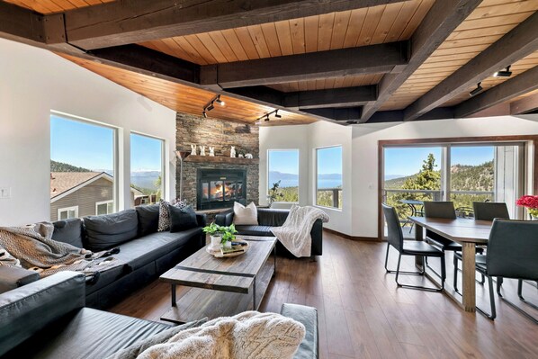A modern living room with a fireplace, large windows, and a dining area.
