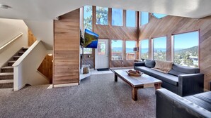 A modern interior with a staircase, a sofa, a coffee table, and large windows offering a view of the outdoors.