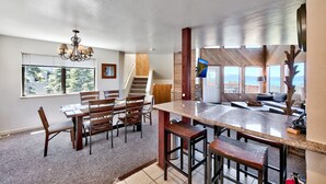 A spacious kitchen with a granite countertop, wooden chairs, and a dining table. A staircase leads to a lofted area with a view.