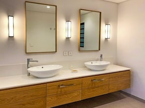 A modern bathroom with two sinks, wooden cabinetry, and wall-mounted mirrors with lighting. - The Waterclub by Horizon Holidays (Black River)
