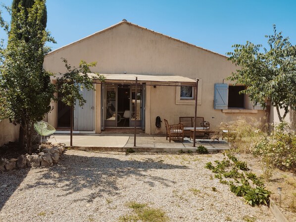 A single-story building with a covered patio, a small garden, and a seating area with a table and chairs.
