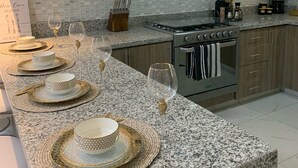 A modern kitchen with granite countertops, stainless steel appliances, and a dining area set with fine china and wine glasses. - Brand New Beach House-- Terrace Beach View (Rosarito)