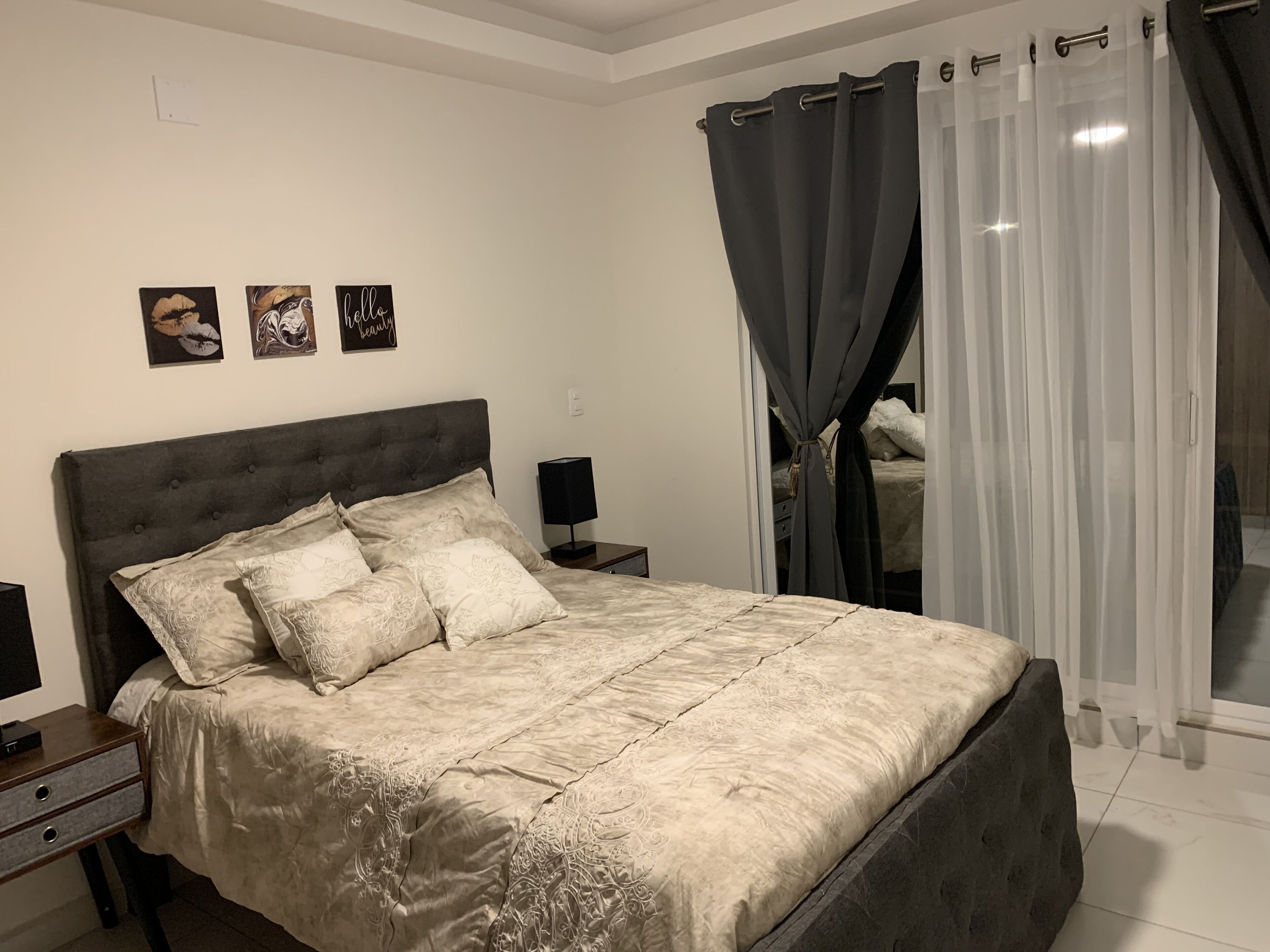 Une chambre à coucher avec un grand lit, une table de chevet avec une lampe et une fenêtre avec des rideaux.