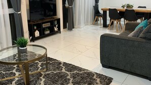 A modern living room with a sofa, a glass coffee table, a TV, and a dining area with chairs and a table. - Brand New Beach House-- Terrace Beach View (Rosarito)