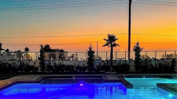 A swimming pool with a blue-lit deck area, surrounded by palm trees and a sunset view. - Brand New Beach House-- Terrace Beach View (Rosarito)