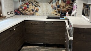 Une cuisine moderne avec des meubles de couleur bois foncé, un plan de travail blanc et un revêtement mural décoré d’un motif représentant un panier de fruits.