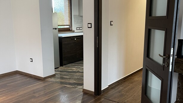 Un intérieur moderne avec un plancher en bois, un coin cuisine doté d’une fenêtre et une porte donnant sur une autre pièce.