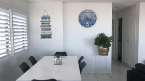 Un comedor con una mesa blanca, sillas negras, un reloj de pared y un letrero colgante con varias frases.