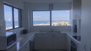 Una cocina moderna con un amplio ventanal que ofrece vistas al mar y edificios.