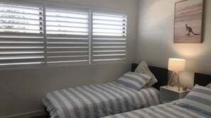 A bedroom with two beds, a nightstand with a lamp, and a wall-mounted picture. - Kings Beach Apt: Ocean Views & Rooftop (KINGS BEACH)
