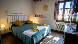 Une chambre à coucher avec un lit, une table de chevet, une lampe, une fenêtre et un radiateur.
