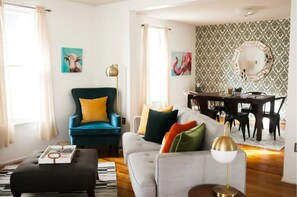 Ein Wohnzimmer mit einem türkisfarbenen Sessel, einem grauen Sofa und einem Essbereich mit einem dunkelholztischen und Stühlen.