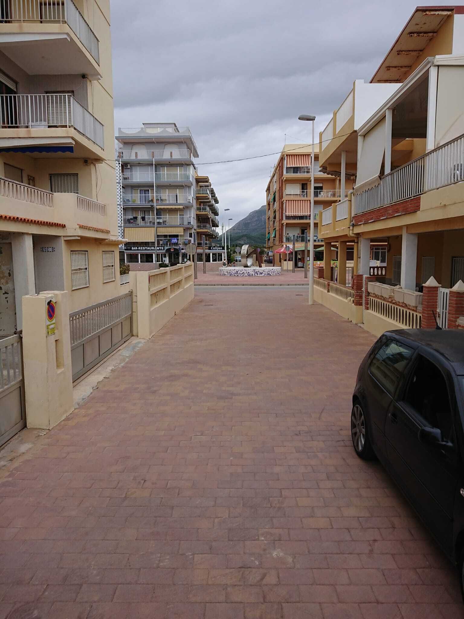 Une rue bordée de bâtiments des deux côtés, une chaussée pavée et une voiture garée.